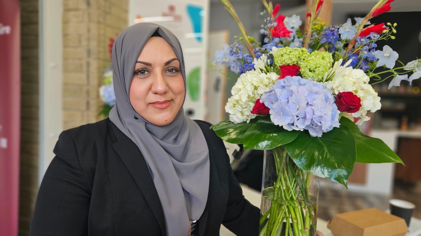 Safeena Khan wears a grey hijab and holding a vase full of flowers.