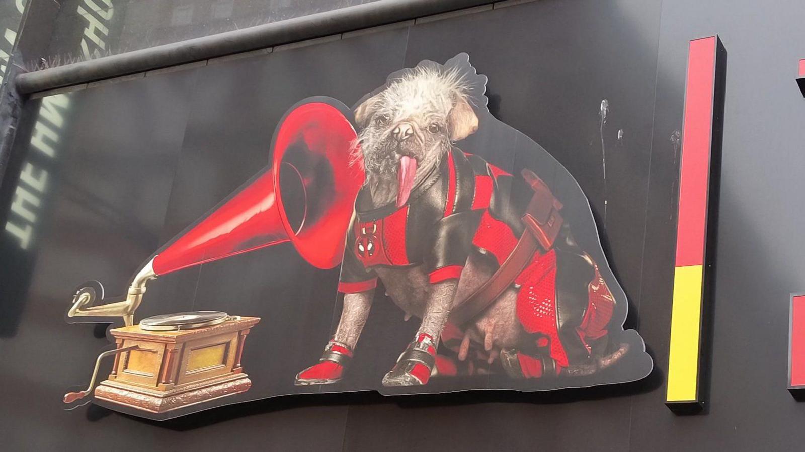 A close-up image of the HMV dog and gramophone logo, with the traditional dog replaced by Peggy in her red and black Deadpool outfit, on the sign of a store in Oxford Street, London's image