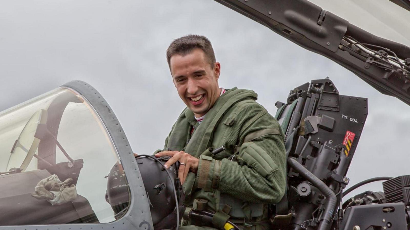A pilot in a green flying suits smiles as he sits in the cockpit of an RAF jet, with the canopy raised above his head.