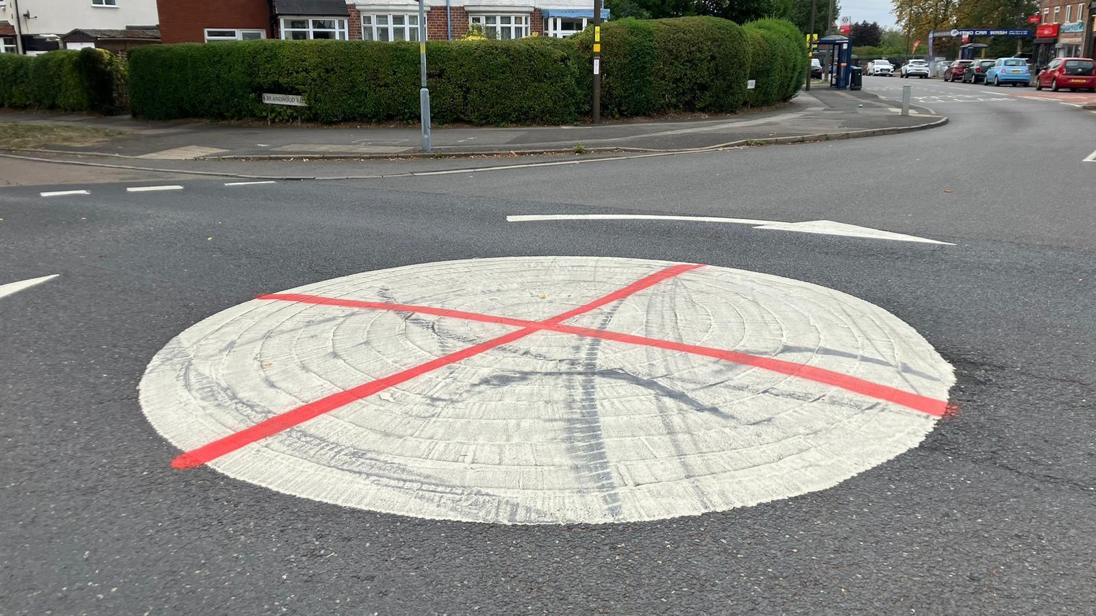 A large white mini roundabout circle in the middle of two roads. It has been vandalised with red spray paint to look like an England flag