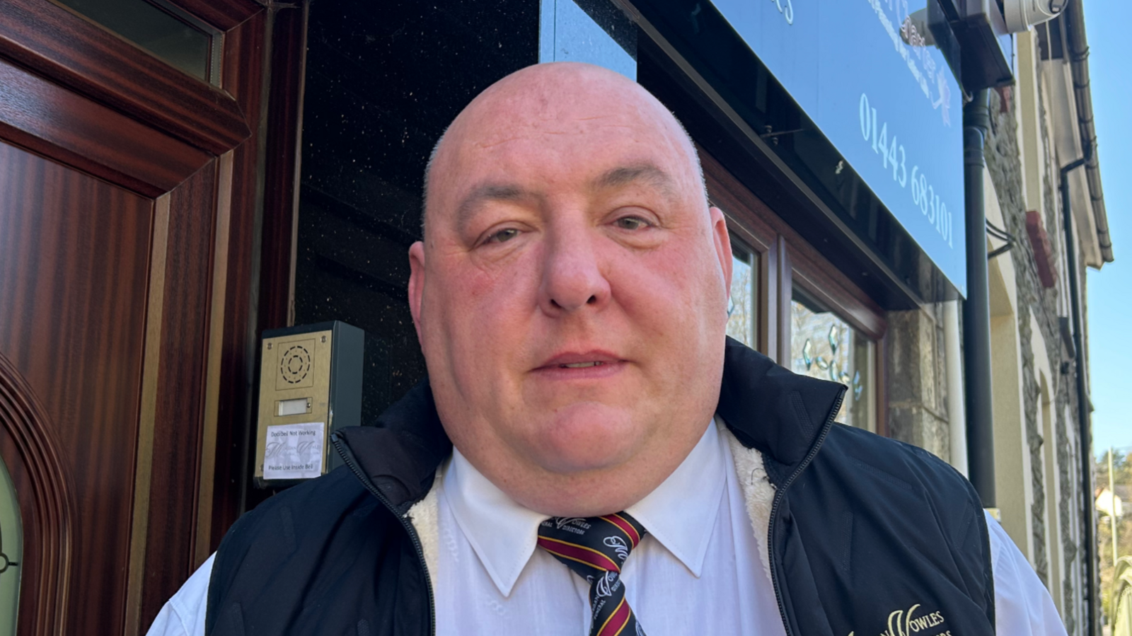 Geraint Griffith is a bald man wearing a gilet, white shirt and red and blue striped tie 