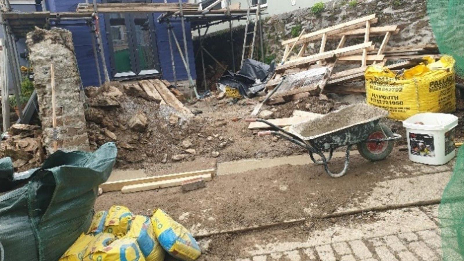 One of the back gardens in the early stage of restoration. The house is scaffolded, there are mounds of earth and broken masonry. There are also builders' dumpy bags, bags of concrete, wooden frames and a wheelbarrow. 