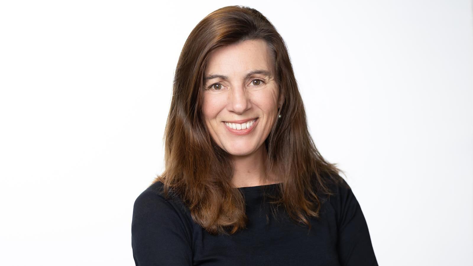 Photo of Tanya Tracey, CEO of Girls are Investors. She has long brown hair, is wearing a black long sleeved top and is smiling at the camera.