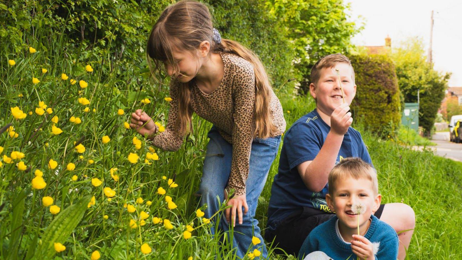 Three children on grassy bank with flowers