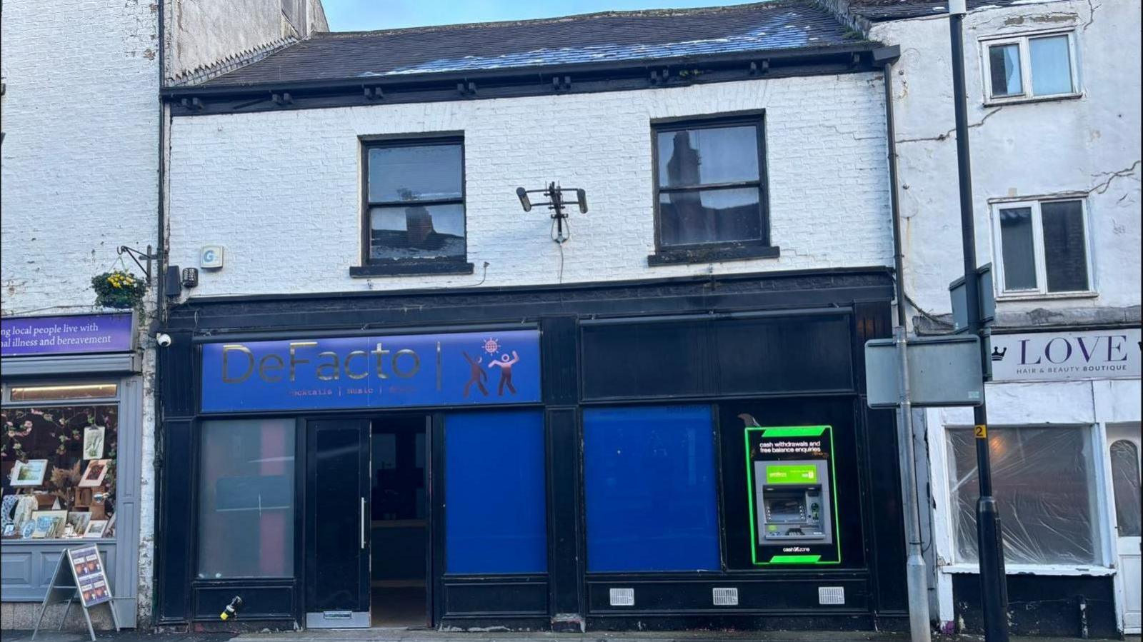 De Facto nightclub on North Street in Ripon - black paintwork with a blue sign. Snow on the pavement in front. Shops to the left and right.