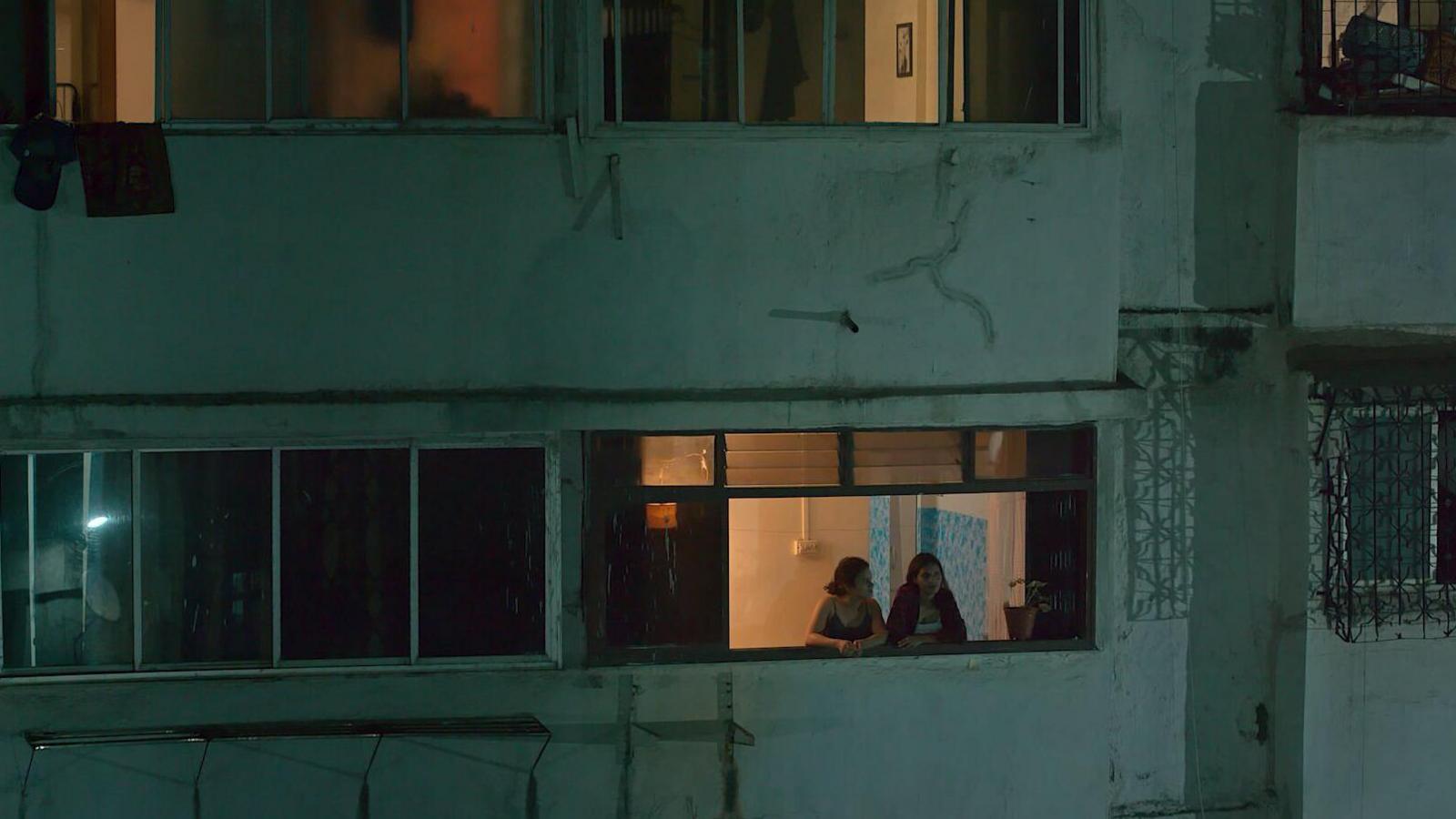 Two women looking out of an apartment block window at dusk.