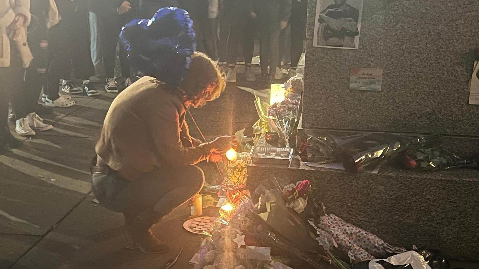 A person holding a blue balloon crouches down next to the statue where flowers and tributes have been placed in Liam Payne's memory.