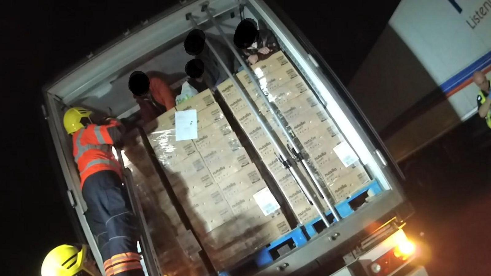 A firefighter is on a ladder helping men who are sat on pallets of Nutella chocolate spread in the back of a lorry. The faces of the men have been blurred