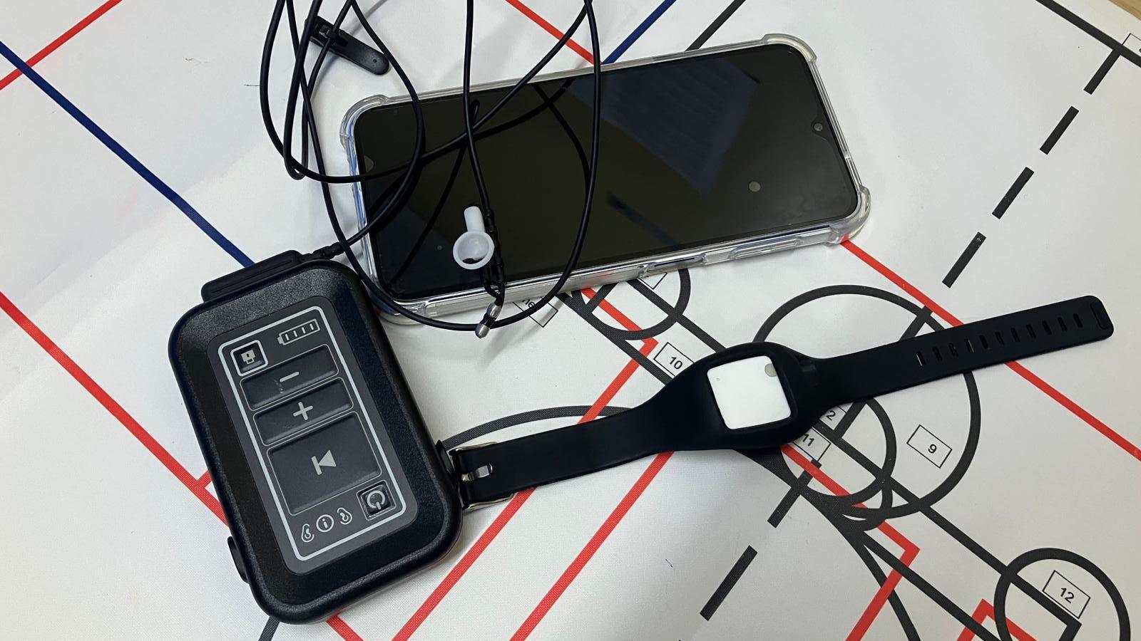 Hospital equipment is laying on a sheet of paper with grids and circles. A pacemaker-like device connects to an ear-piece. A smartphone sits next to the wires.