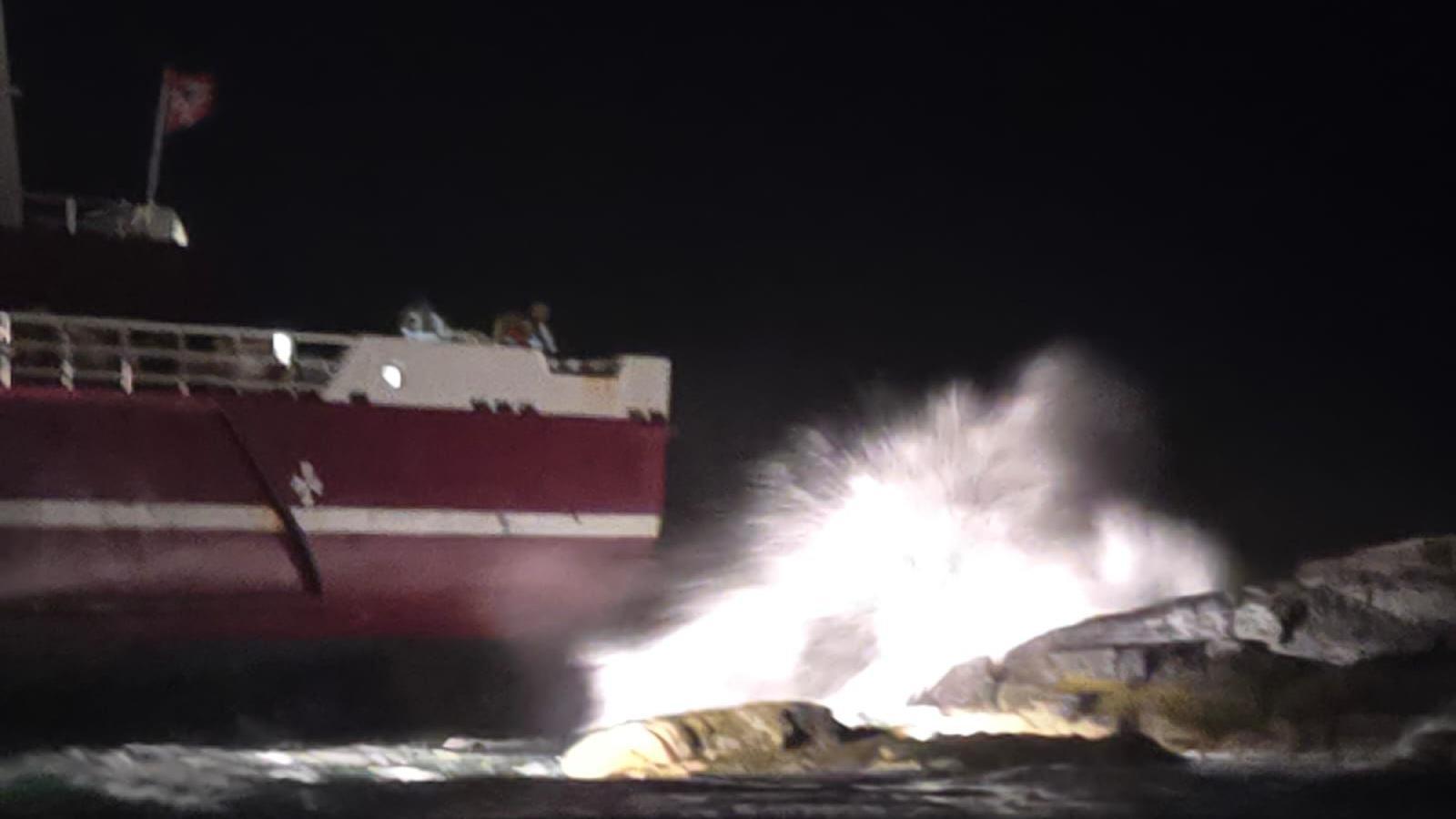 A red and white boat hits the rocks on the Isle of Skye - water is spraying up as a result.