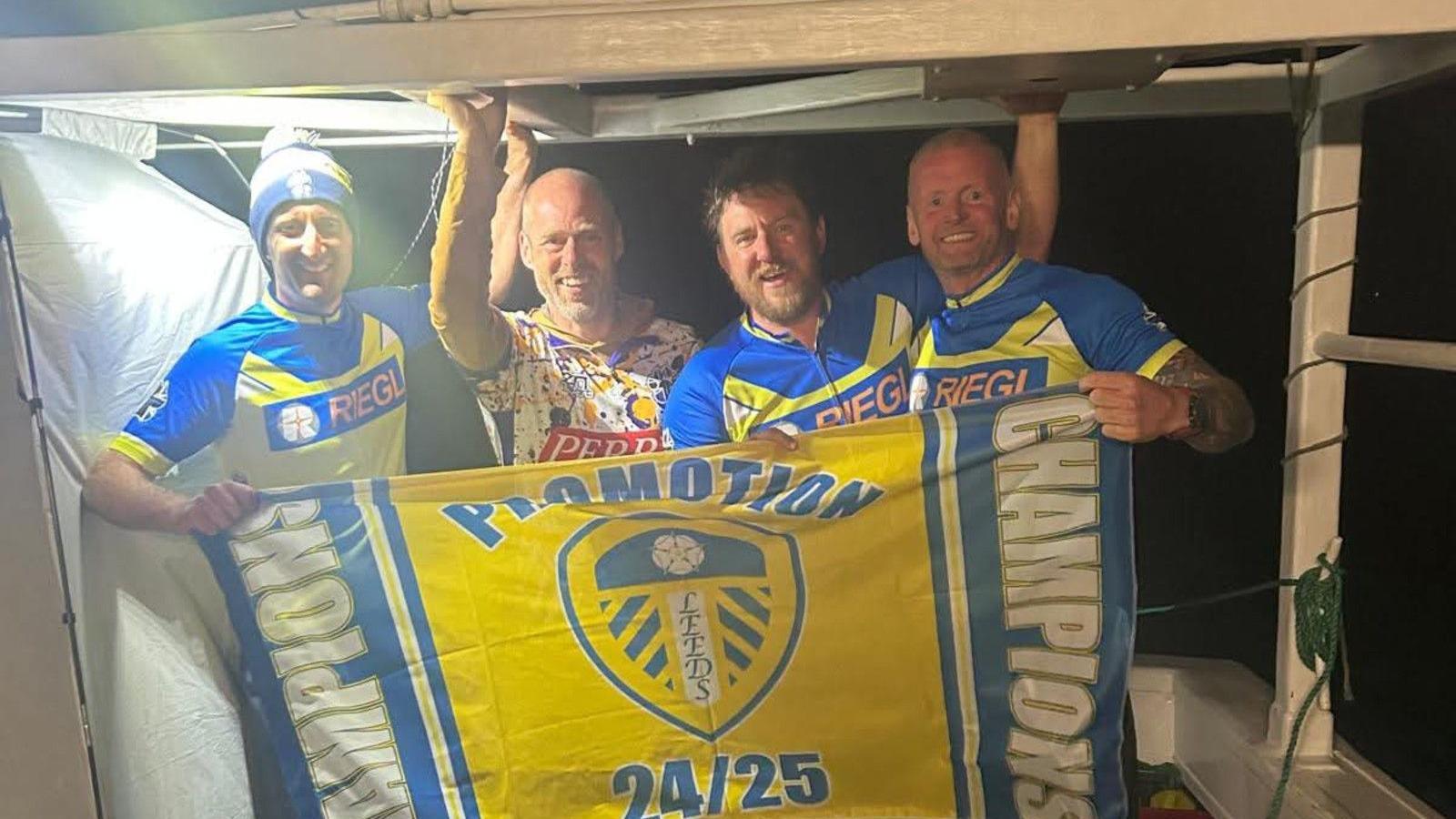Mark Baber, Dave Young, Nathan Pawlowski, and Kevin Lacks-Kelly are pictured on a boat in dark in the English Channel holding a Leeds United flag.