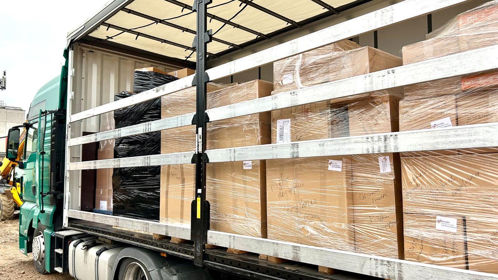 A close up picture of an open lorry filled with cardboard boxes that are piled on top of each other. 