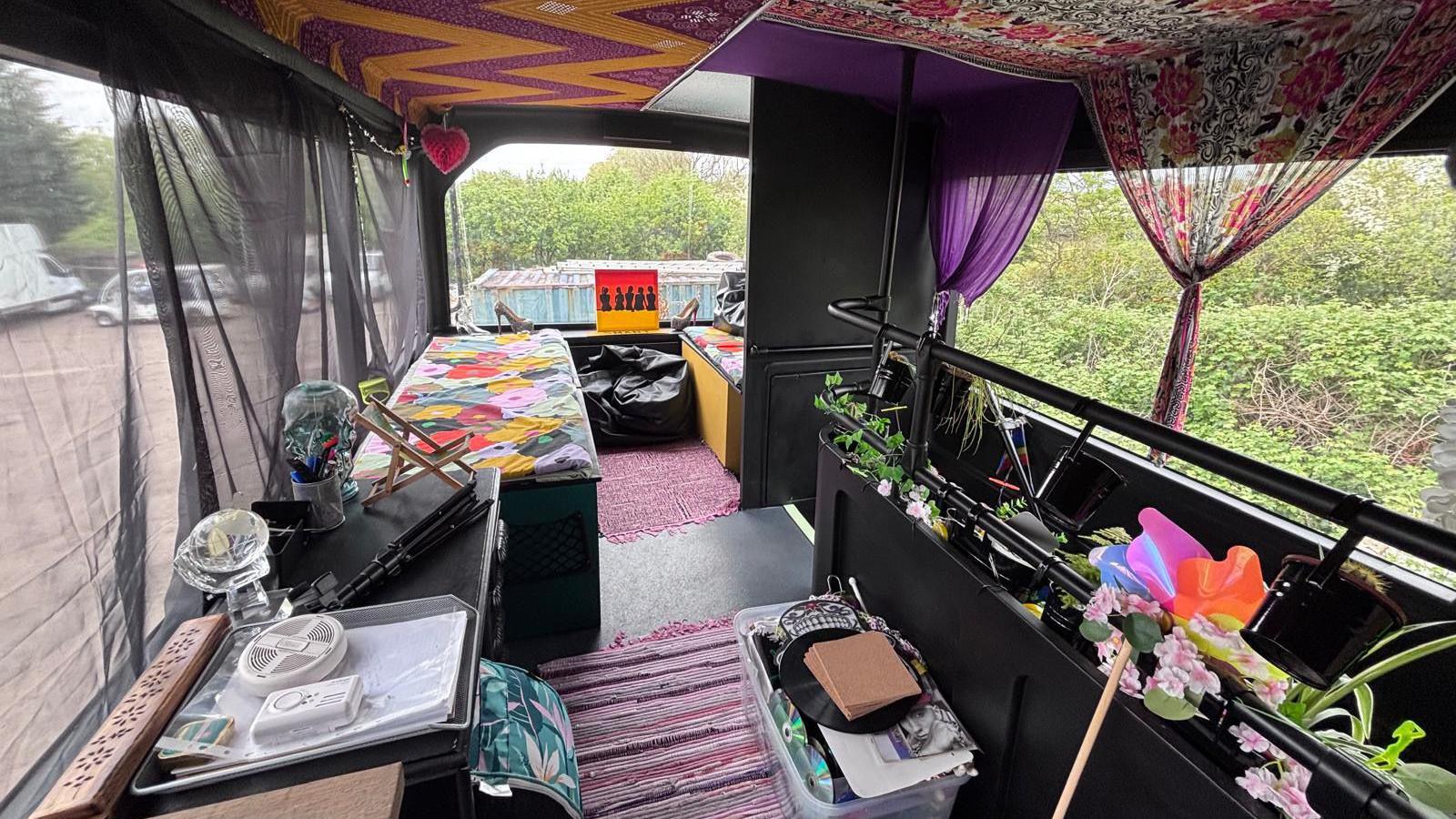 An interior view of the double decker bus' top deck. It has colourful furniture and decorations.