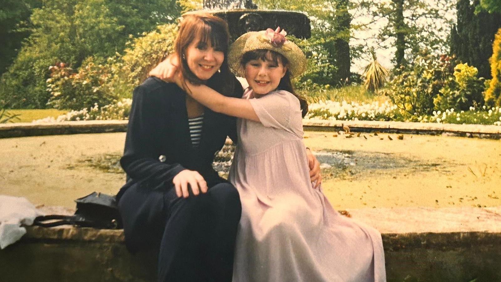 A woman holds her daughter on a wall of a water fountain 