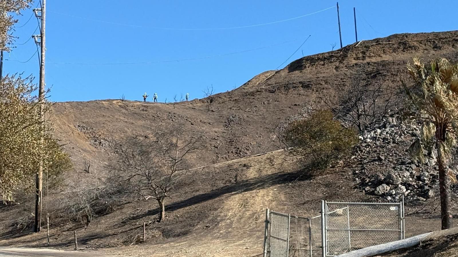 Workers are seen on a ridge line in a scorched area of Temescal Canyon