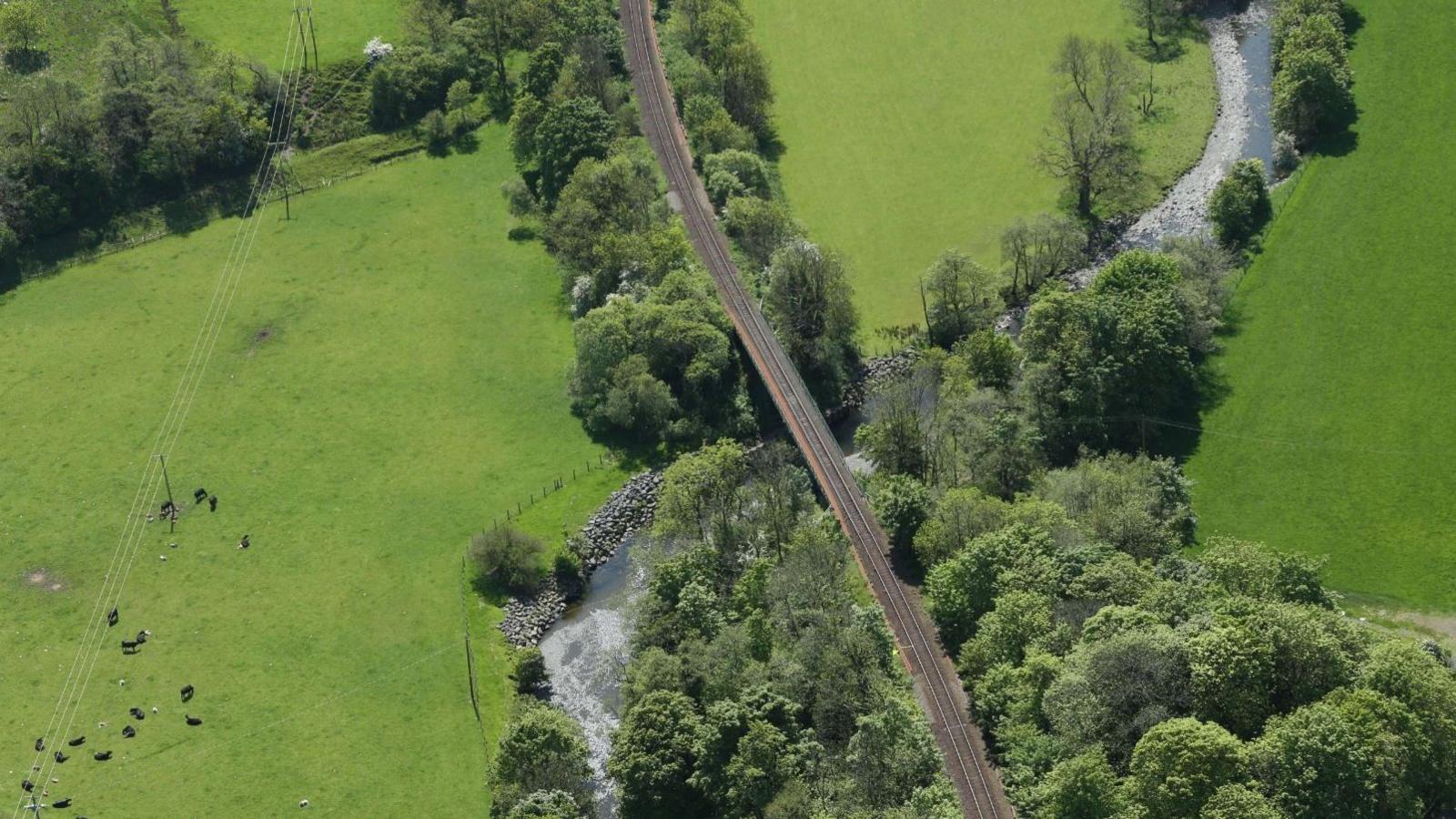 An aerial view of the Stranraer to Ayr railway line passing over a river with trees and fields around it
