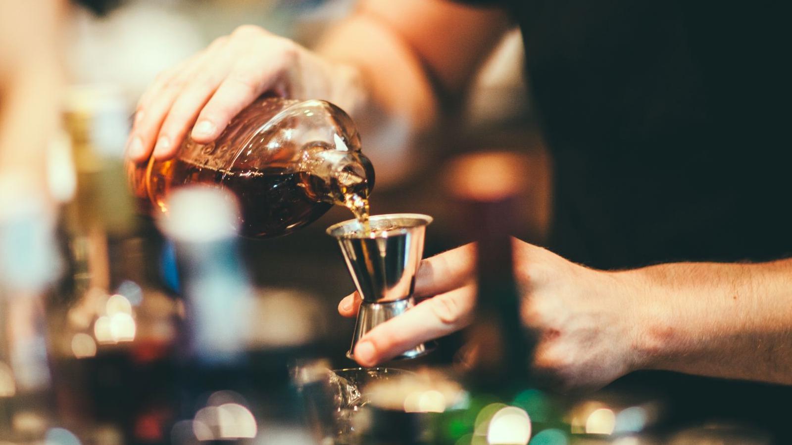 A bar worker pours liquor into a measure