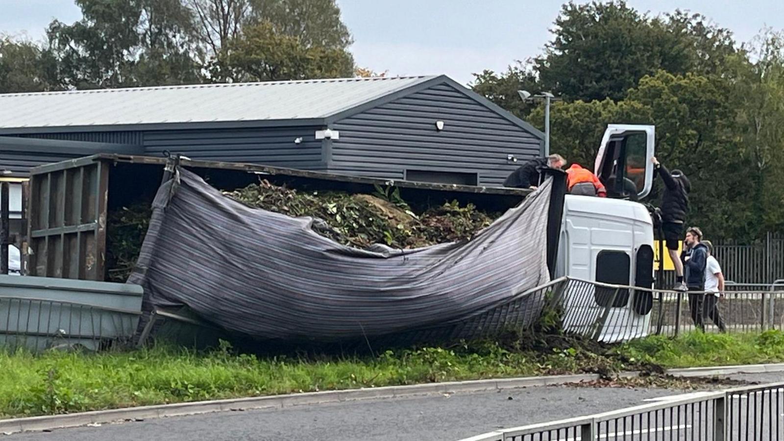 People climb onto the cab of a lorry lying on a central reservation railing