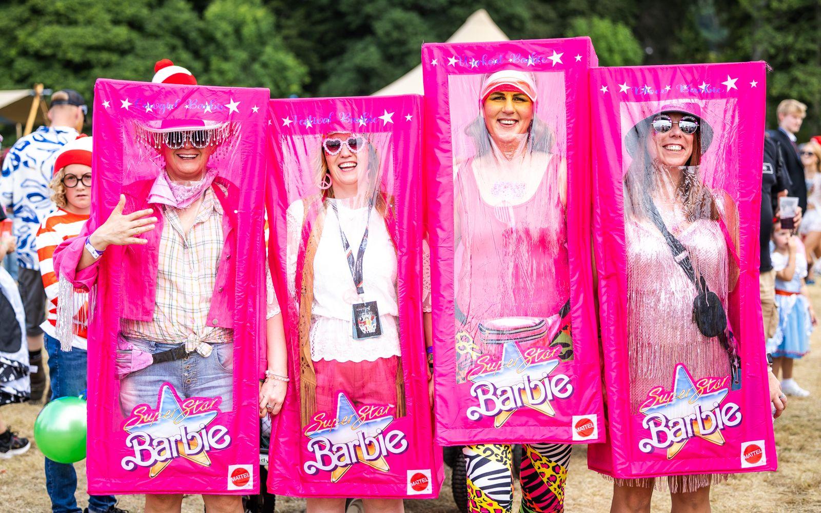 Four people dressed as Barbie dolls, inside oversized pink Barbie doll box