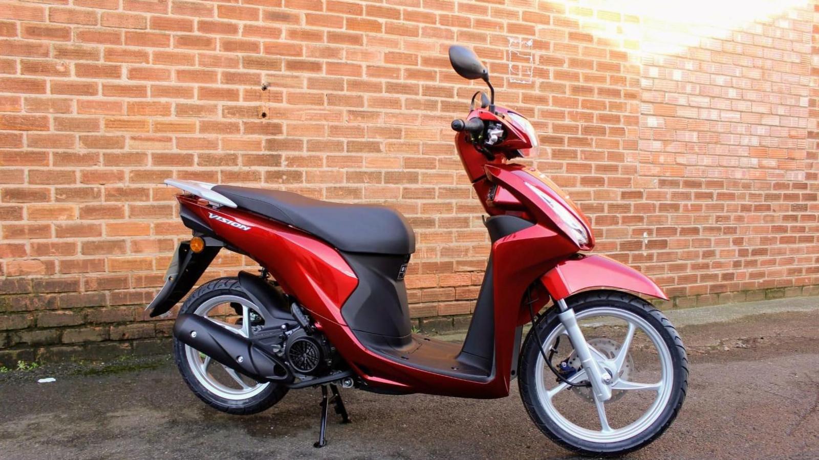 A red moped in front of a brick wall