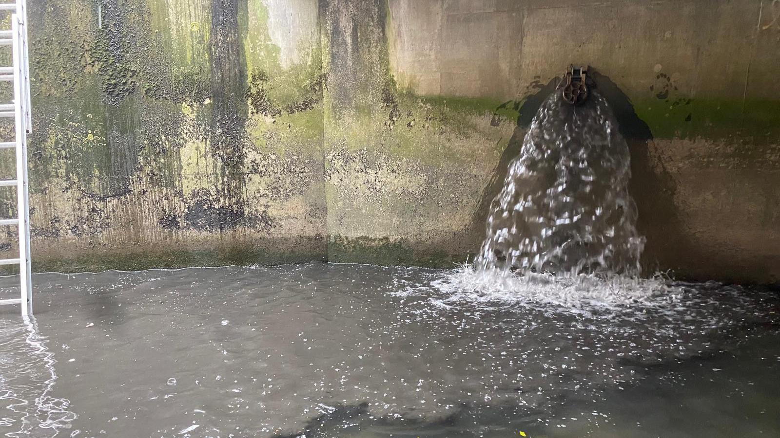 A grey spout of water is dropping into the river