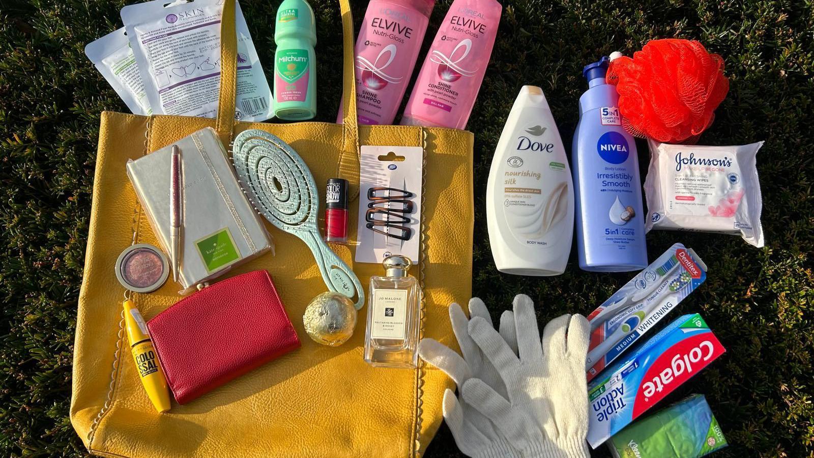 A yellow handbag surrounded by dozens of personal items including mascara, hairbrush, woolly gloves, hairgrips and nail polish