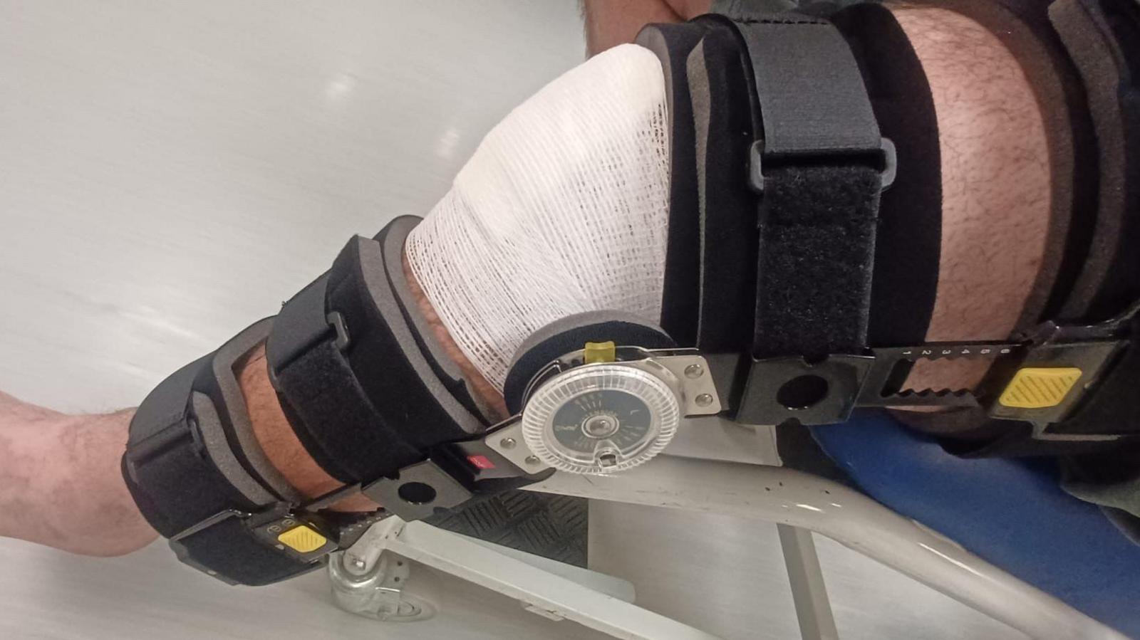 A close up of Stephen's leg in a brace with a bandage over his knee. He is sat in a wheelchair.