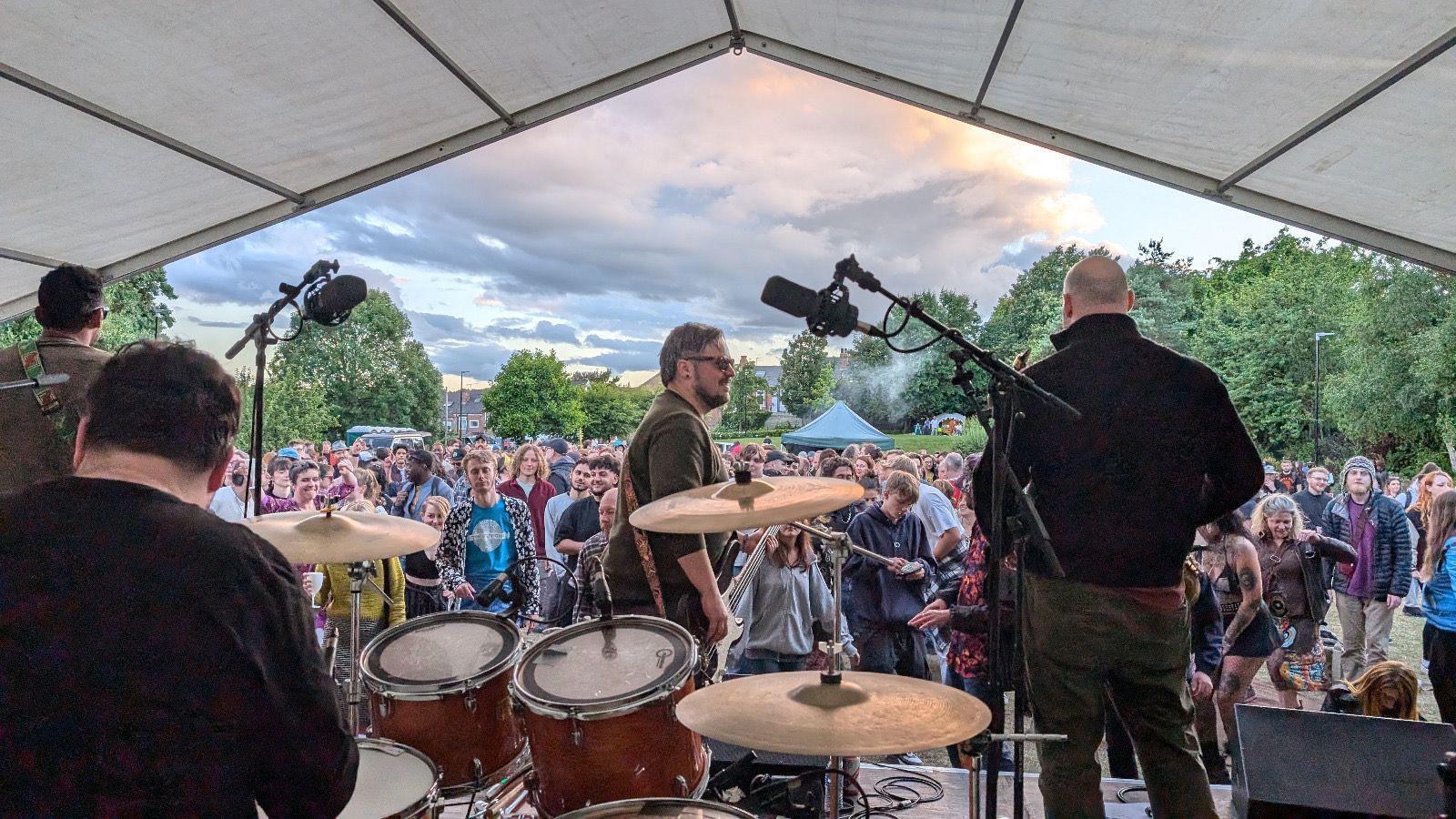 A view from the stage of people gathered at the festival, with a live band performing in front of them.