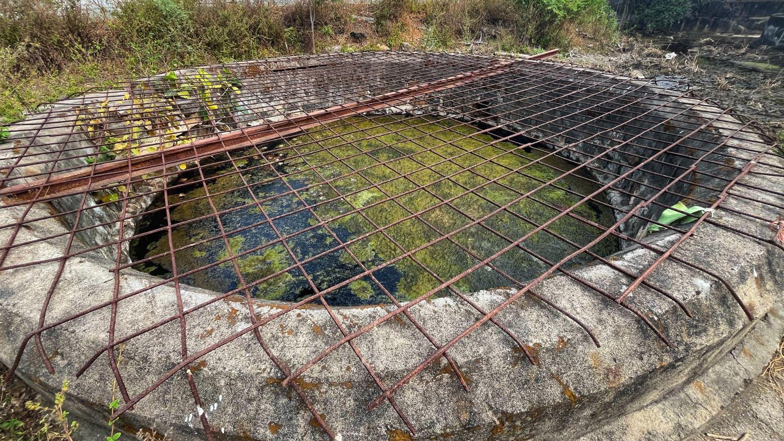 A picture of a well with algae floating on top and a steel grill, with water contaminated by chemicals due to rapid industrialisation.