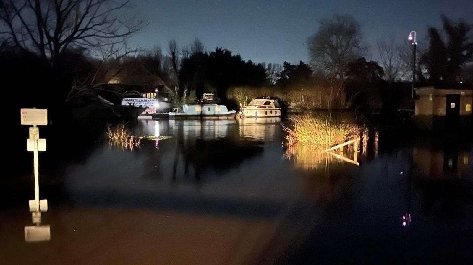 A night-time shot of a flooded marina with three boats in the background. 