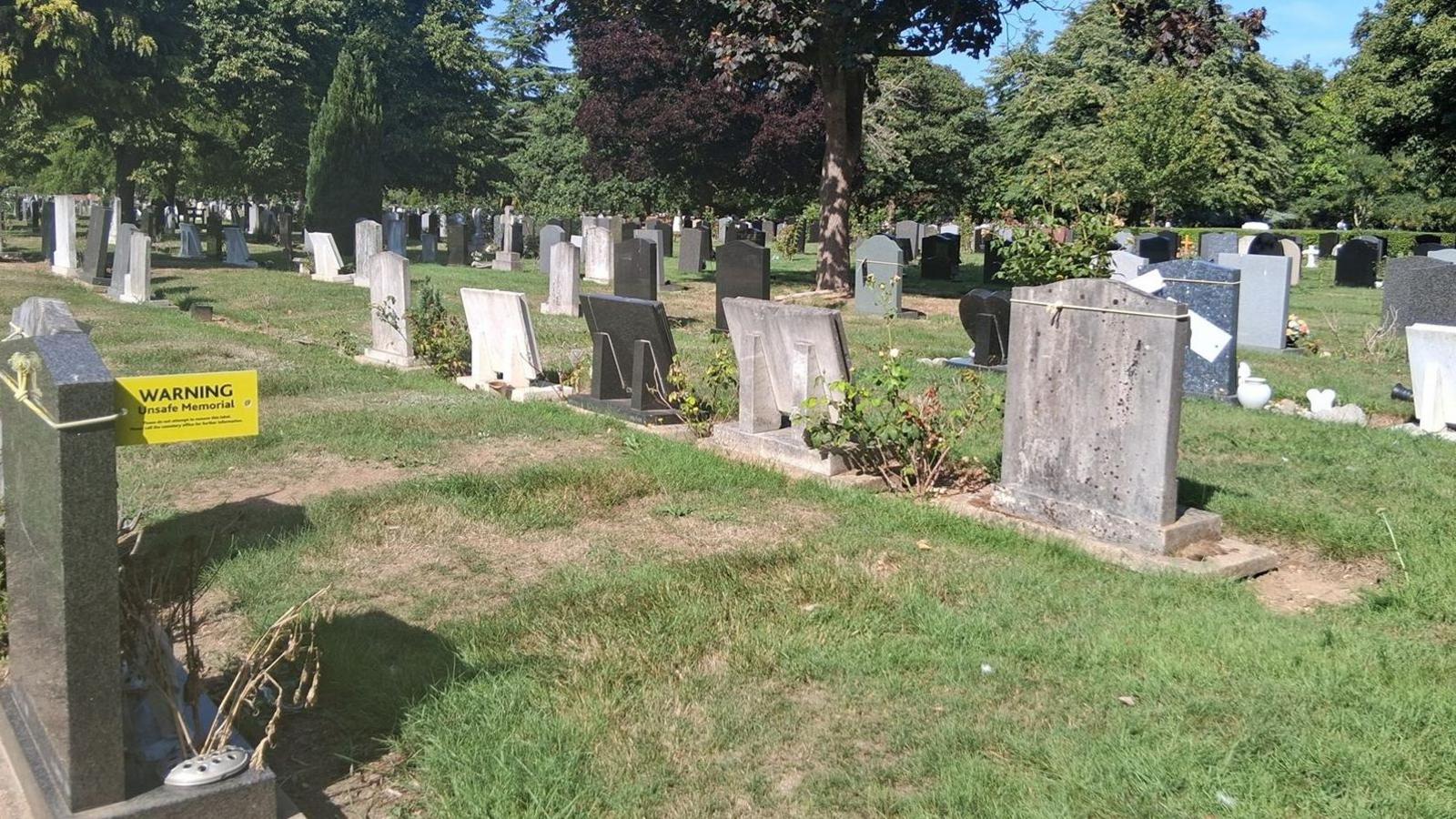 A cemetery with gravestones. The gravestones are in rows, with grass all around, and trees in the background.
