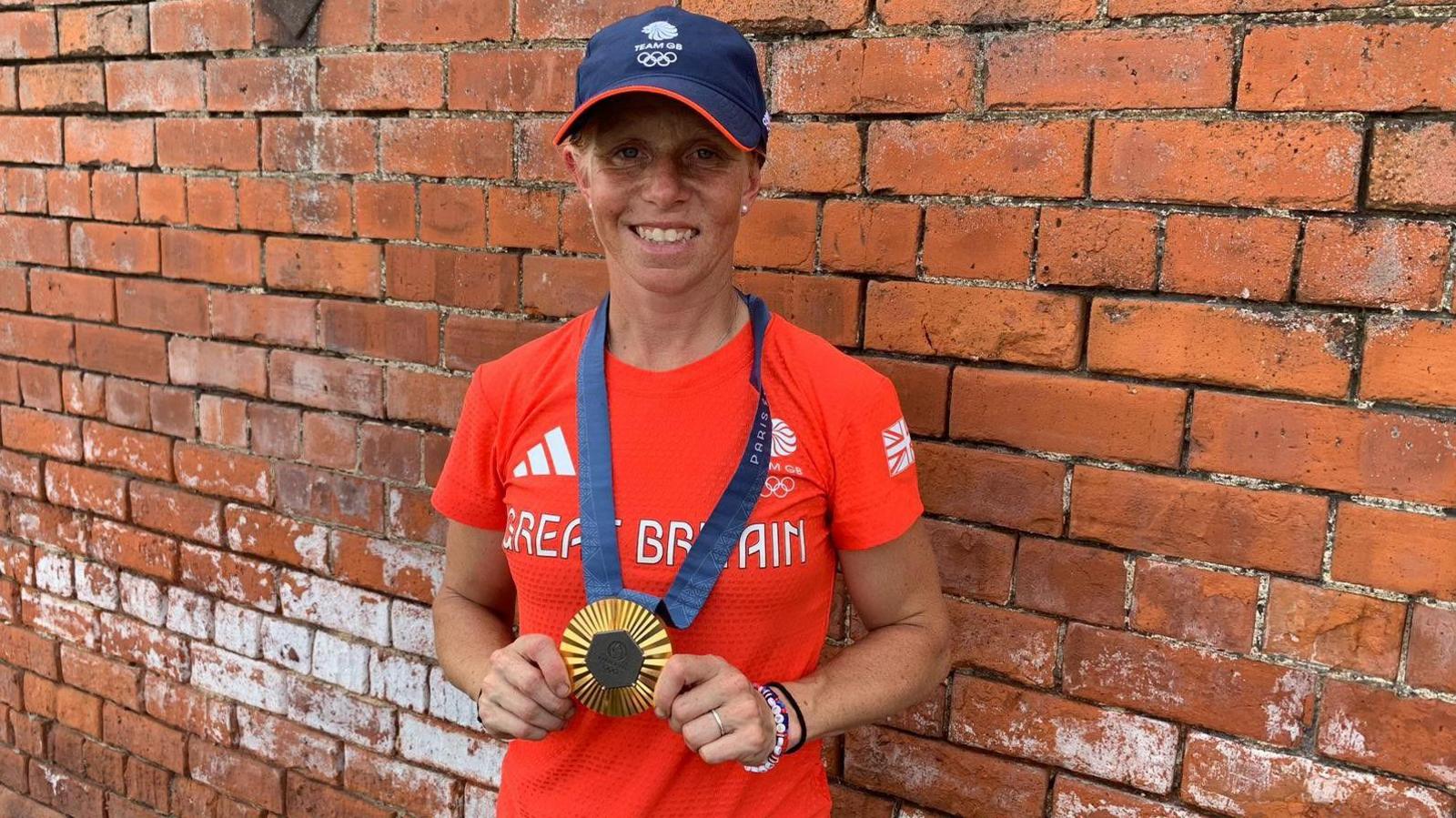 Ros Canter wears a Team GB t-shirt and proudly holds her gold medal as she poses against a brick wall at her family farm 