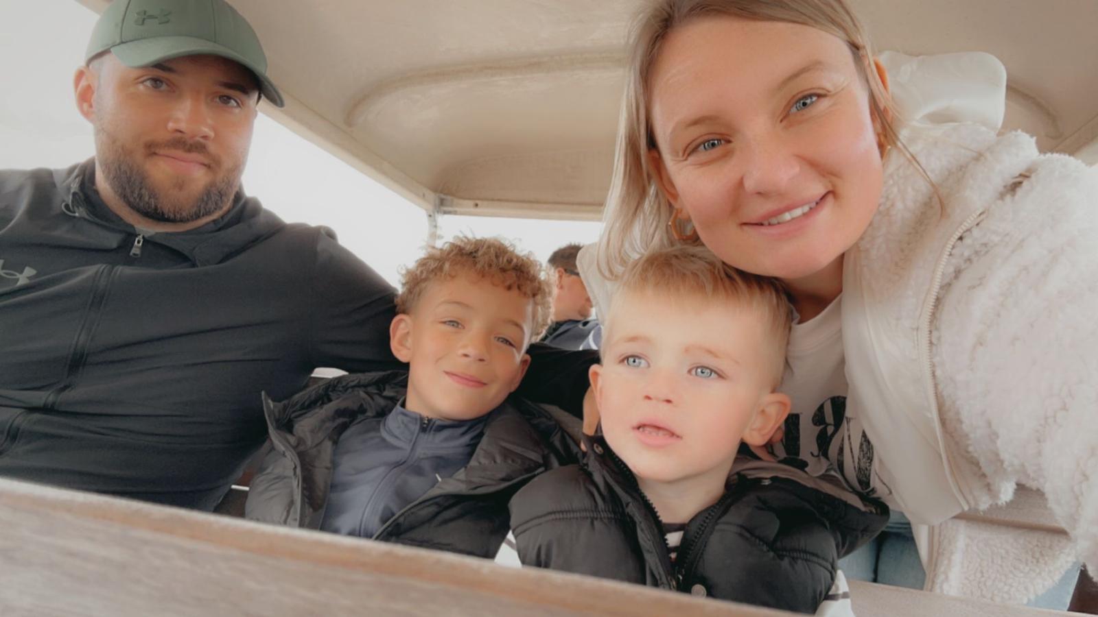 A family of four, a man, a woman and two young boy smiling at the camera