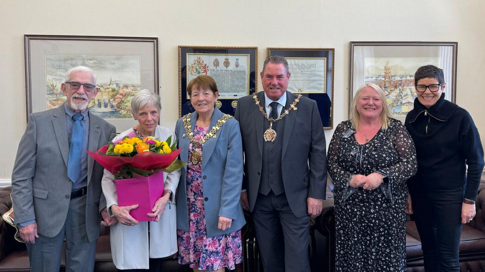 Sue and Pete Williams hold flowers dressed in formal clothing as they stand next to dignatries from Tameside Council for a presentation. 