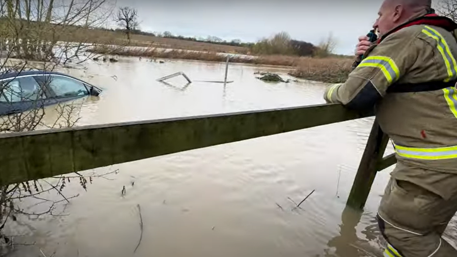 A firefighter talking on a walkie talkie while looking at a partially submerged car