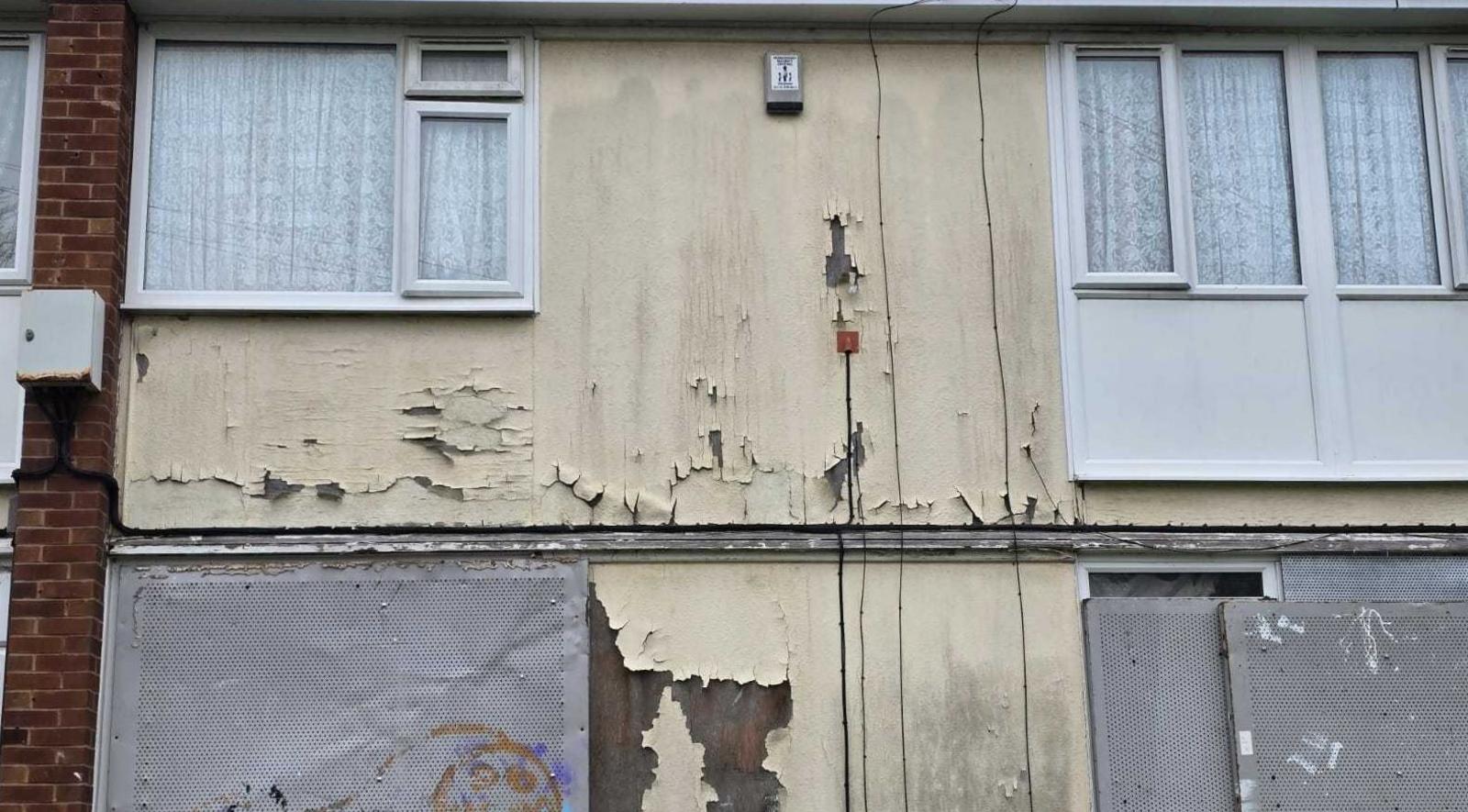 Picture of a boarded up house. Metal sheets cover the windows and paint is coming away from the front of the property.