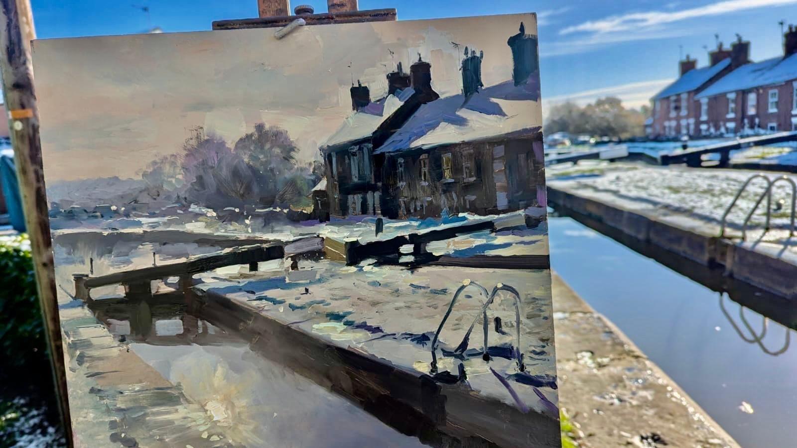 A painting of a canal lock, in place in front of the actual scene depicted. In both the painting and photo, a row of terraced houses are visible on the other side of the canal. 