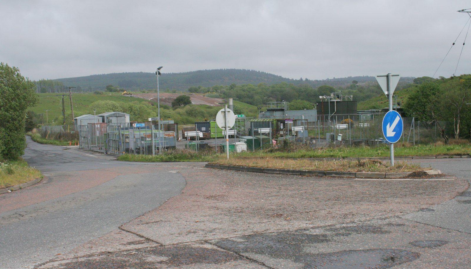 A council recycling site viewed from a distance with a fence round it and many containers inside