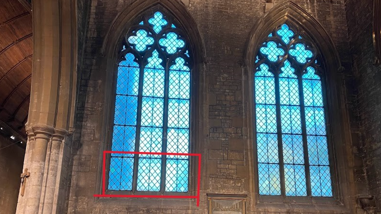 Two large glass windows inside the church, the window on the left has three panels at the bottom of the window highlighted in red, this shows where the stained glass will be reinstalled. 