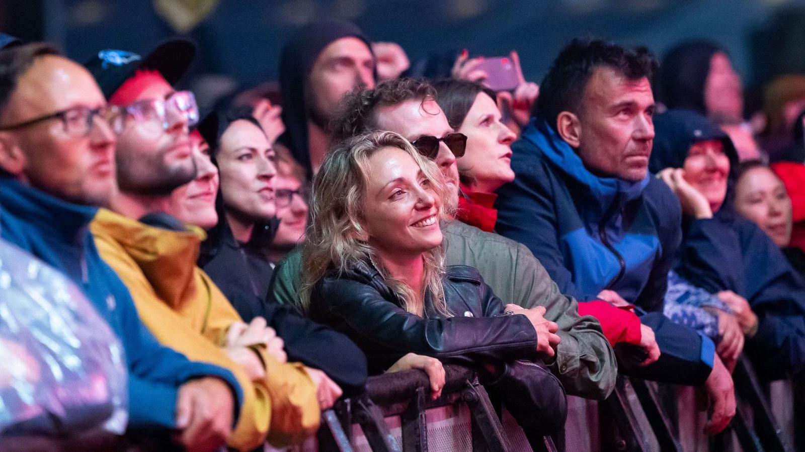 The front row of fans at the Massive Attack concert on The Downs in Bristol lean on the barrier as they watch the band. Many of them are wearing waterproofs