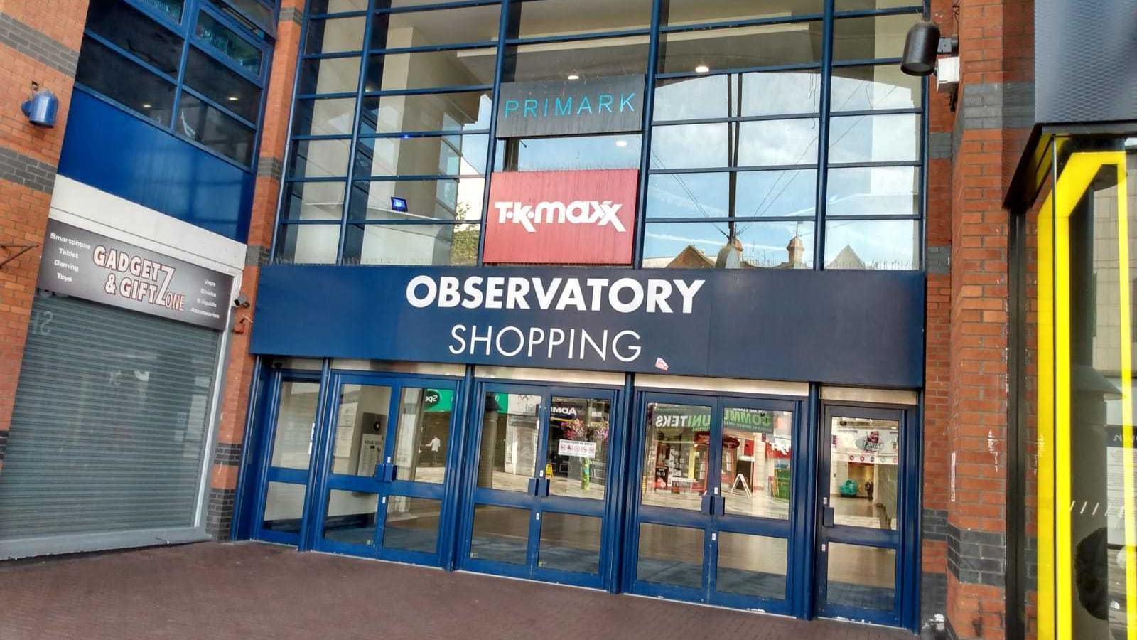 A row of three double glass doors with a blue and white sign above them saying 'Observatory Shopping'.