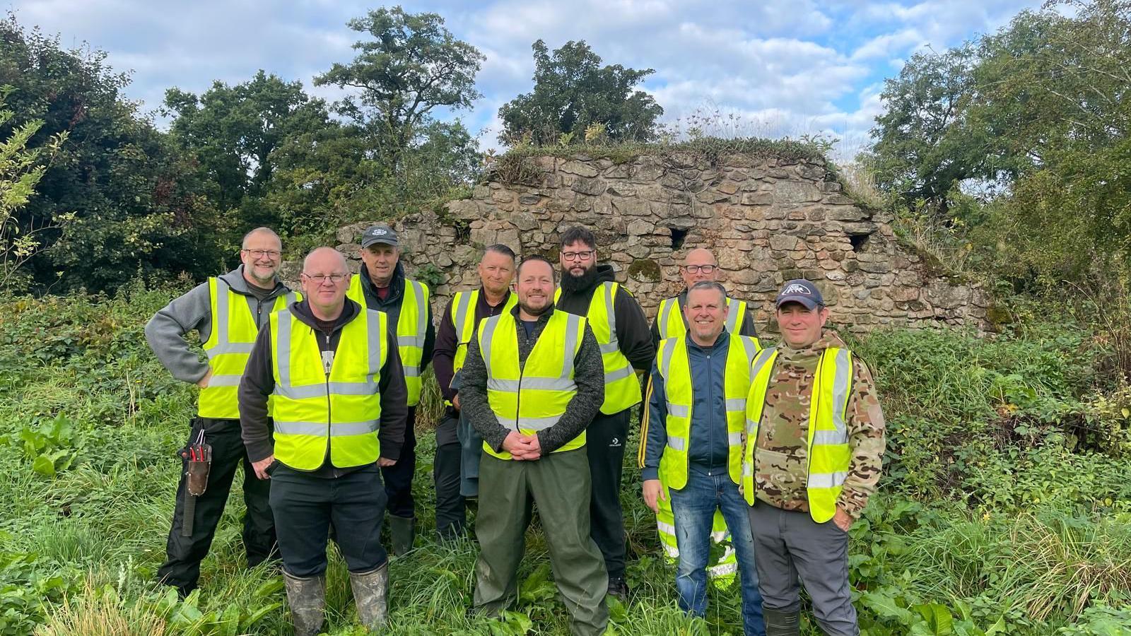 A group of men in high viz vests standing in front of a ramshackle wall