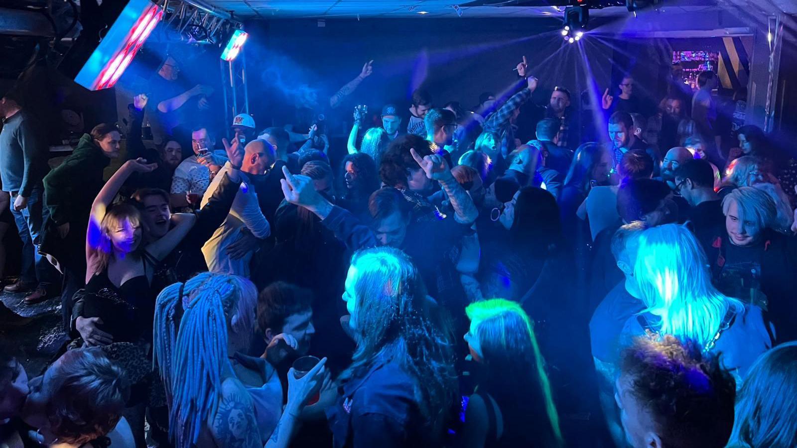 A huge group of people dancing in a club, bathed in blue light.