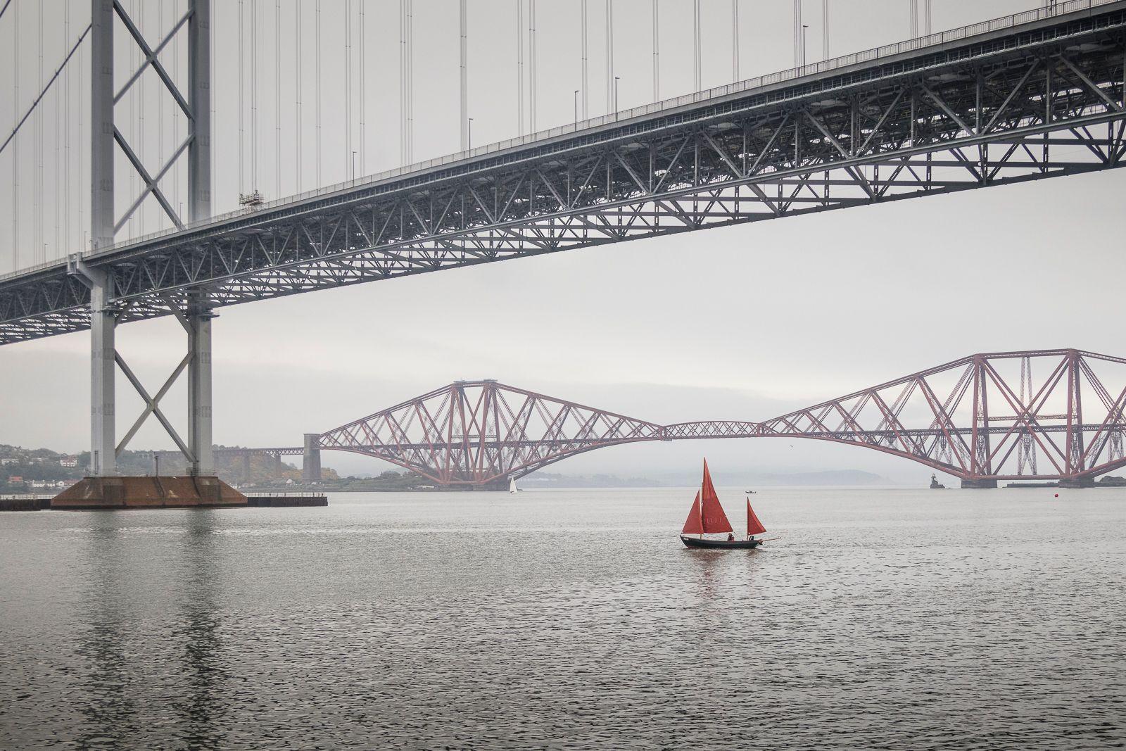 Sailboat with a red sail below the Forth Road Bridge