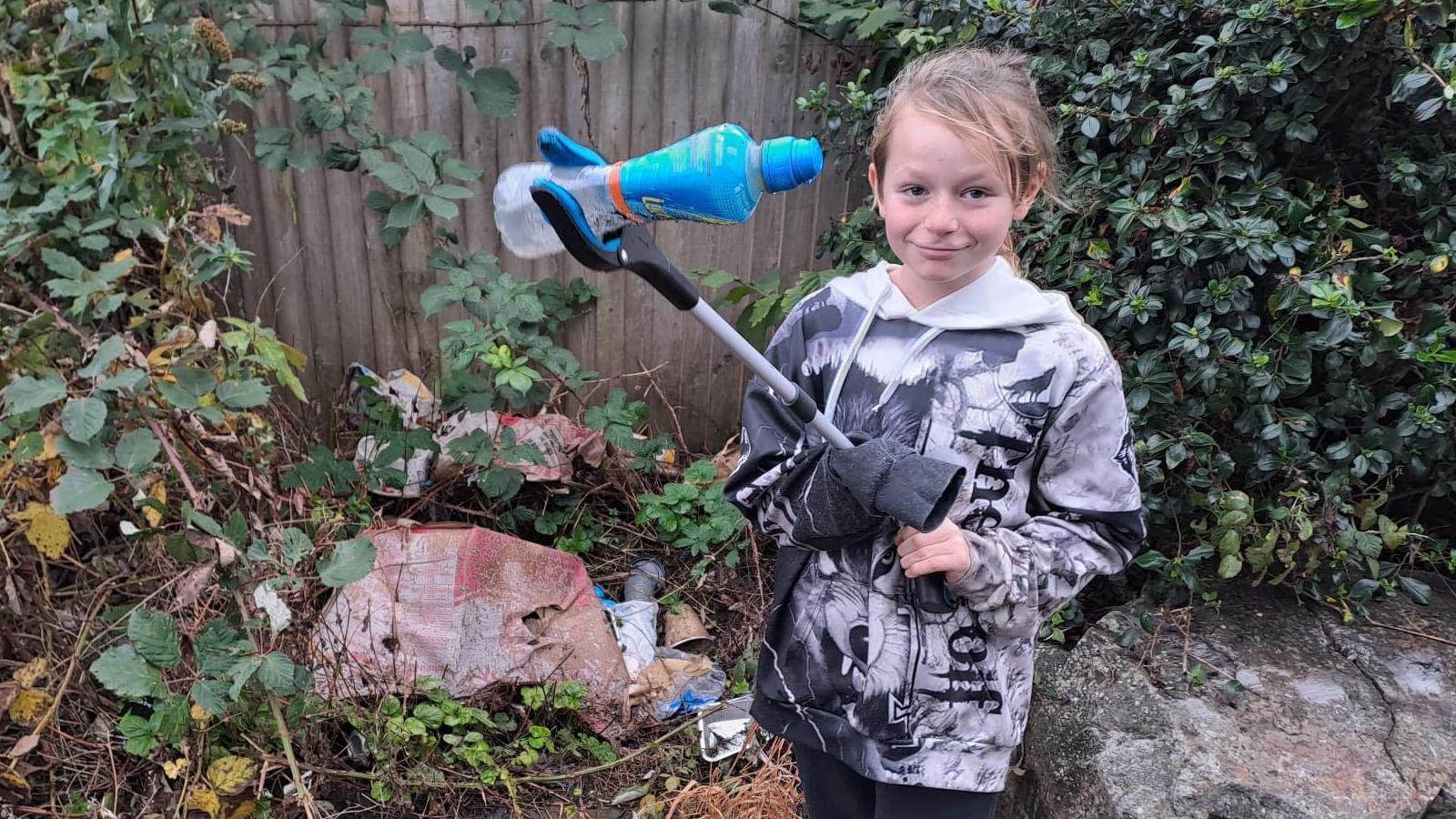 Image of nine year old Theo out picking up litter using a pair of grabbers to hold up an empty plastic bottle