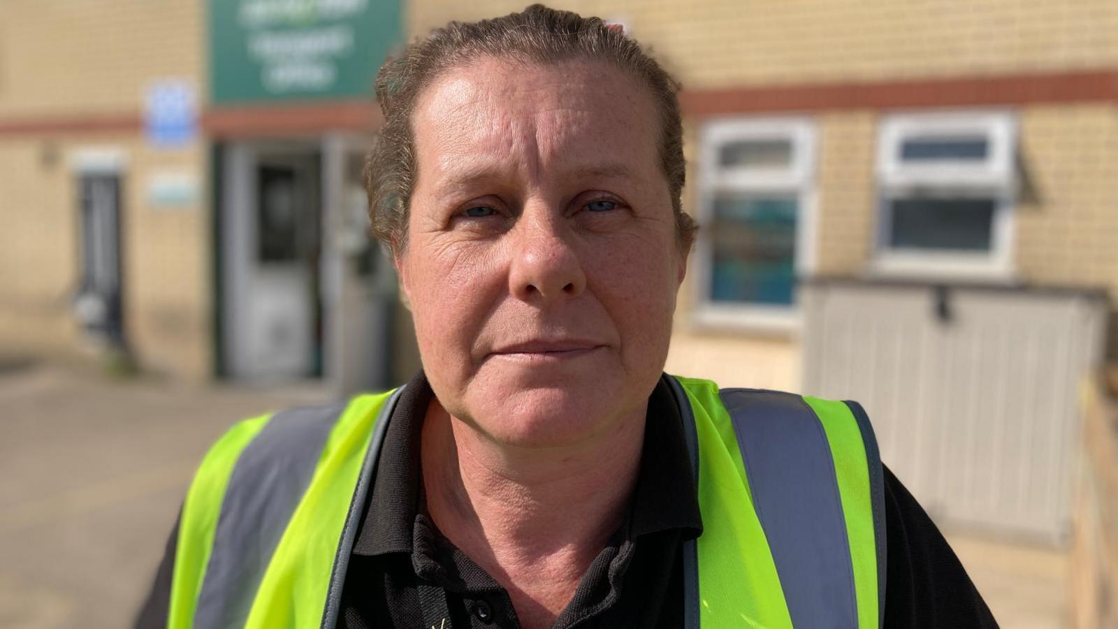 A head and shoulders photograph of Lindsay Burrows of Branston Potatoes.  She is wearing a hi-visibility jacket and is standing in a yard. She has short dark hair swept back.