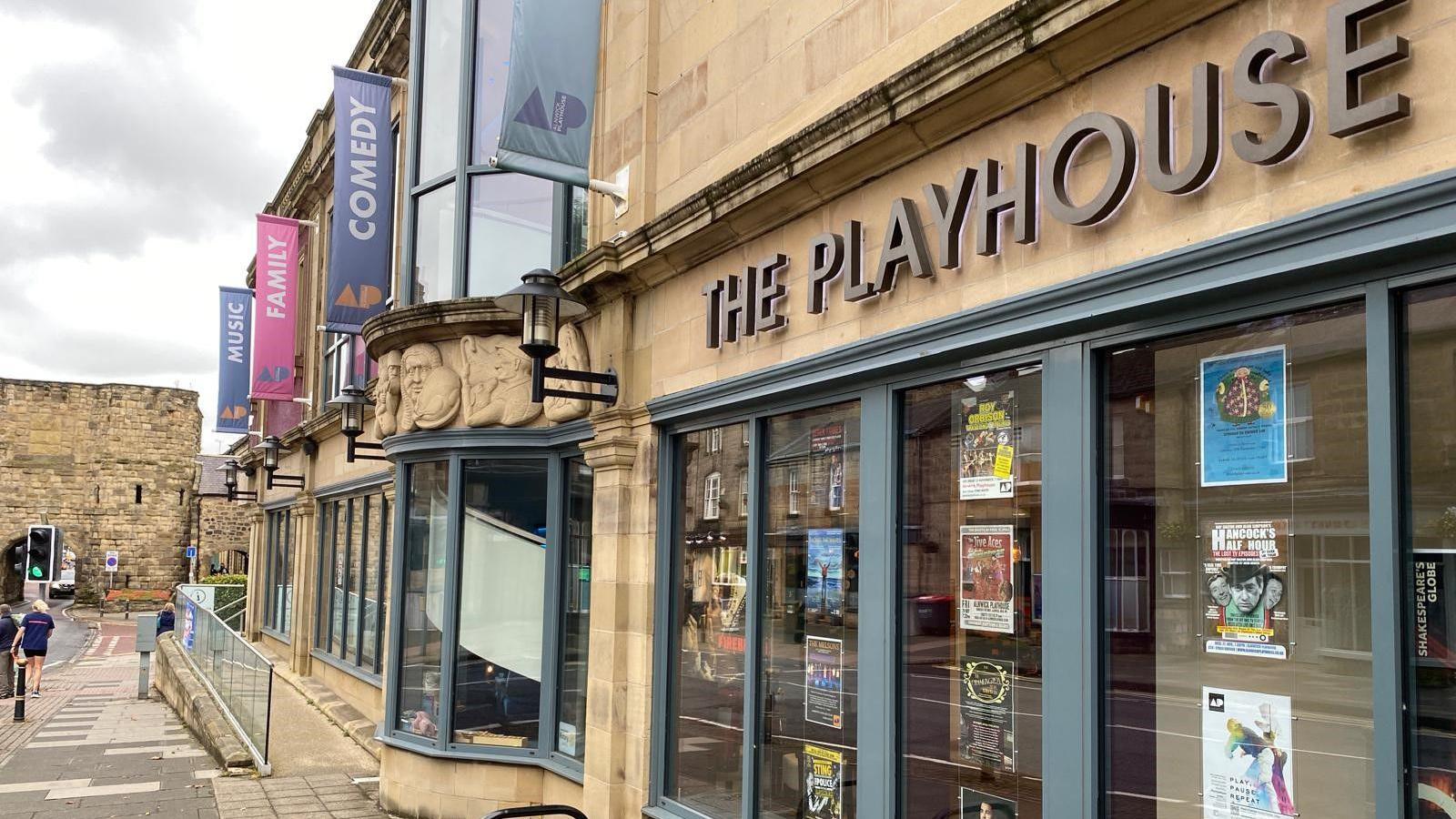 The exterior of Alnwick Playhouse, a Georgian sandstone building with flags outside and a number of windows. At the bottom of the image you can just make out Alnwick's Bondgate Tower.