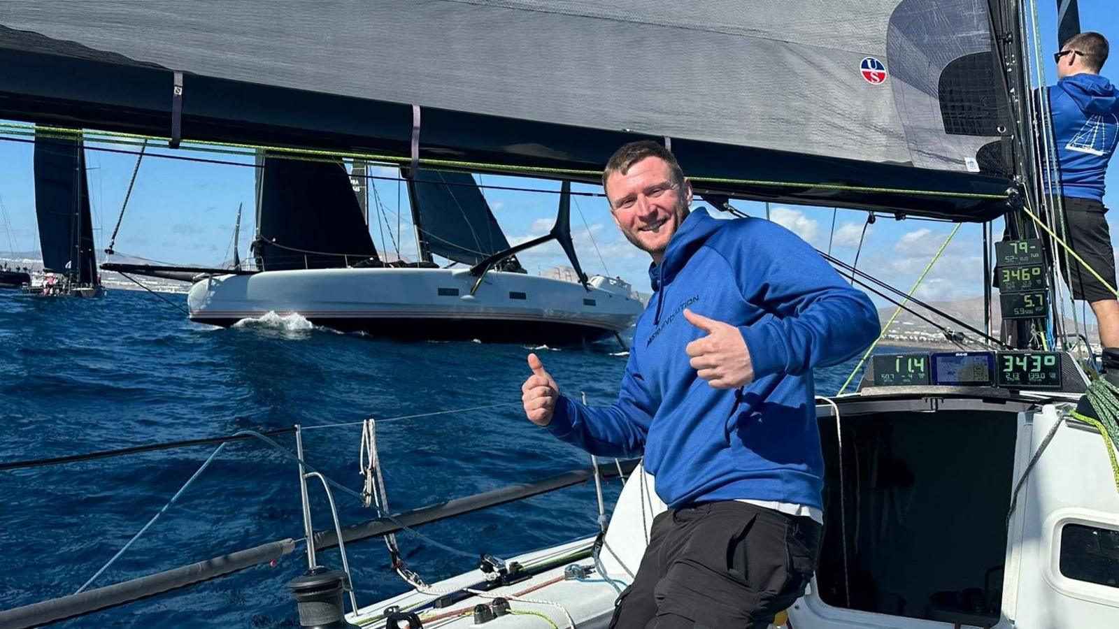 Llun o Thomas ar y cwch yn barod i gychwyn y ras