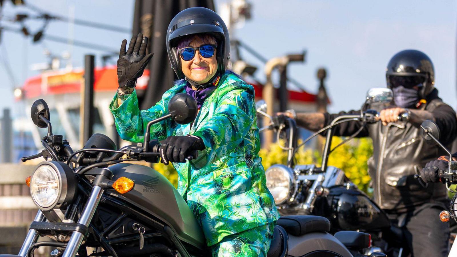 A woman in a green suit riding a black motorbike.