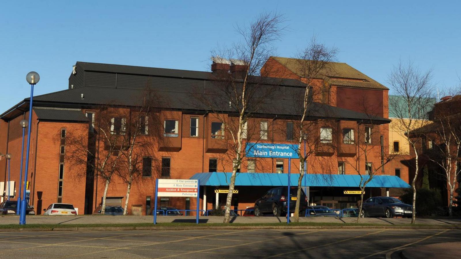 A view of the exterior of Scarborough Hospital, a red brick building with a blue canopy over the entrance. 